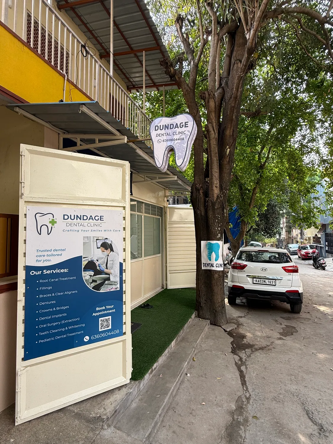 Dundage Dental Clinic entrance and tooth-shaped sign beside the tree-lined pavement